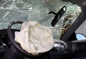The interior of a car with a deployed airbag, shattered windshield, and broken rearview mirror suggests a recent collision or accident with potential vehicle injuries.
