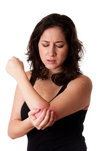 Woman with medium-length brown hair wearing a sleeveless black top, holding and rubbing her left elbow with a pained expression, suggesting discomfort or injury possibly due to a recent motor accident. Woman with medium-length brown hair wearing a sleeveless black top, holding and rubbing her left elbow with a pained expression, suggesting discomfort or injury possibly due to a recent motor accident.