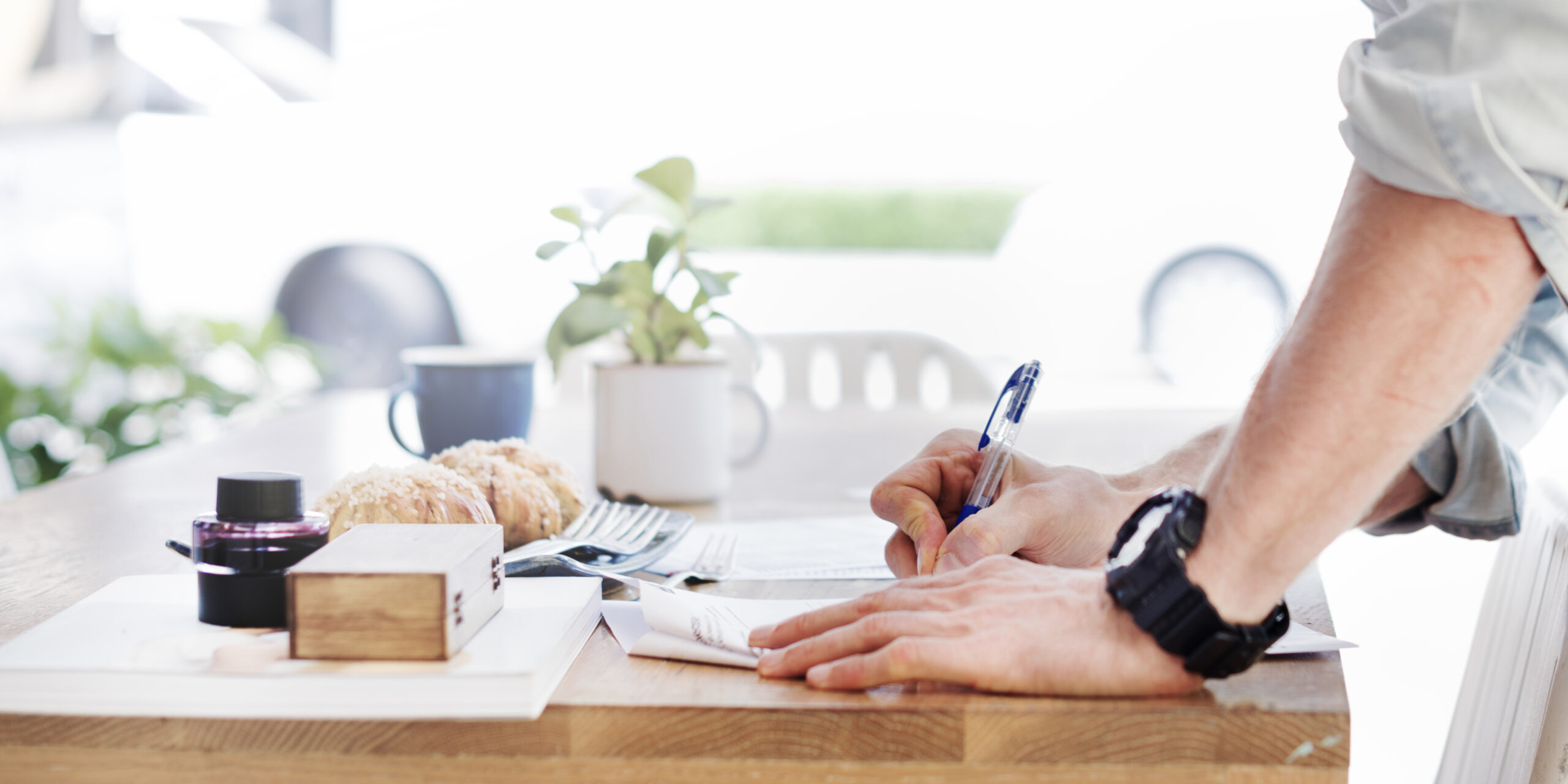 Side view of hand writing on paper on wooden table with bakery